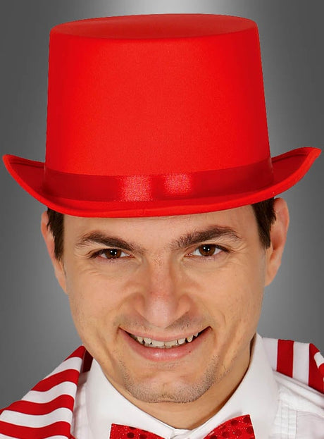 Ein Mann, der einen roten Zylinderhut von Bequemer sowie eine dazu passende rot-weiße Fliege und einen gestreiften Schal trägt und in die Kamera lächelt.