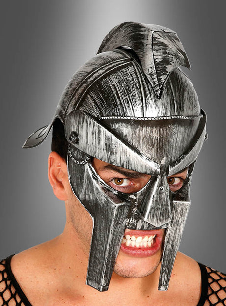 Eine Person, die den „Gladiator Helm für Männer“ trägt – einen verwitterten, silberfarbenen Kunststoffhelm im Antik-Look mit Helmkamm –, posiert vor einem dunkelgrauen Hintergrund.