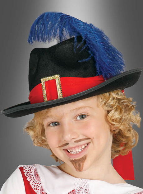 Ein Kind mit lockigem blondem Haar trägt einen Musketierhut für Kinder – einen schwarzen Hut, verziert mit einer blauen Feder und einem roten Band – sowie einen falschen Schnurrbart und einen Ziegenbart und lächelt in seinem Musketierkostüm charmant in die Kamera.