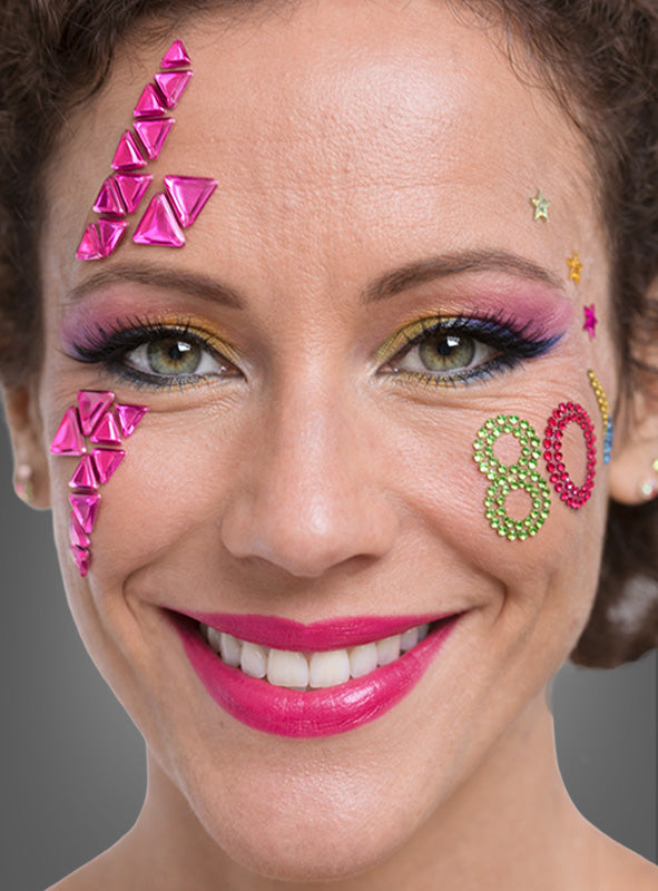 Eine Frau mit auffälligem Make-up, rosa Lippenstift und bunten 80er-Jahre-Schmuck-Tattoo-Glitzersteinen im Gesicht, darunter die Zahl „80“ und geometrische Formen – ein auffälliger Look, inspiriert von den lebhaften Tattoo-Trends der 1980er Jahre und dem Flair von Retro-Accessoires.