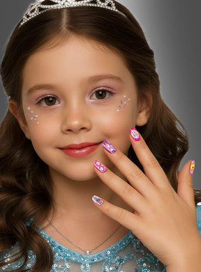 Ein kleines Mädchen mit welligem braunem Haar, gekleidet in ein blaues Kleid und eine Tiara, präsentiert stolz ihre wunderschön verzierten rosa „Kleine Prinzessin Kinder Nägel selbstklebend, 12 Stück“; die selbstklebenden Nägel aus dem Prinzessinnen-Set passen perfekt zu den funkelnden Strasssteinen auf ihren Wangen.