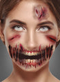 Eine Frau mit realistisch wirkendem Spezialeffekt-Make-up zeigt blutige Wunden an Stirn und Wangen sowie einen aufgerissenen Mund, aus dem Zähne hervorschauen – die ideale Inspiration für das „Schürfwunden-Tattoo mit aufgerissenem Mund“ oder temporäre Tattoos zu Halloween. Grauer Hintergrund.