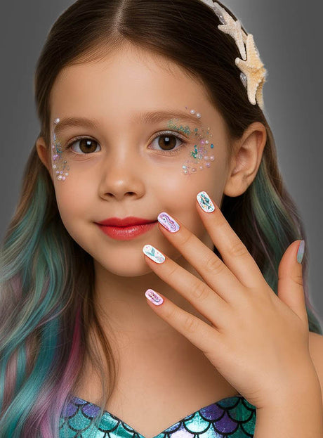 Ein junges Mädchen mit langen Haaren und Gesichtsschmuck lächelt, während es seine Hand zeigt, die mit bunten „Meerjungfrau Kinder Nägel selbstklebend, 12 Stück“ verziert ist. Sie trägt ein Outfit im Meerjungfrauen-Stil, ergänzt durch eine Haarspange in Form eines Seesterns, und präsentiert stolz ihre verspielten Nägel aus dem Set.