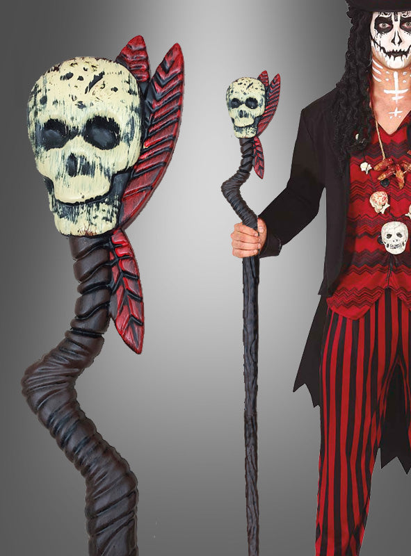 Eine Person, die den „Voodoo Stab 100 cm mit Totenkopf“ in der Hand hält – ein schwarz gewundenes Design mit einem Totenkopf an der Spitze und roten Blättern –, gekleidet in ein auffälliges rot-schwarz gestreiftes Halloween-Kostüm und mit dramatischem Gesichts-Make-up.