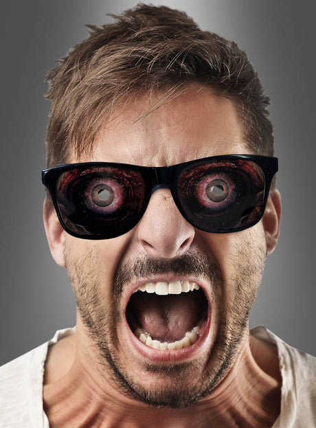 Ein Mann mit Sonnenbrille schreit; anstelle der üblichen Spiegelungen zeigen die Gläser große, gruselige Augäpfel – damit ist diese gruselige Zombie-Brille das perfekte Accessoire für deine nächste Halloween-Party.