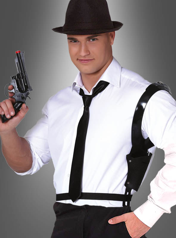 Ein Mann in weißem Hemd, schwarzer Krawatte und Fedora hält einen Revolver in der Hand, während er das Schulterholster „Pistolenholster mit Pistole für Kommissare & Gangster“ sowie Agentenzubehör trägt und vor einem grauen Hintergrund mit Farbverlauf steht.