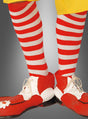Eine Person, die rot-weiße Ringelstrümpfe und Clownsocken sowie übergroße rot-weiße Clownschuhe zu einer gelben Hose trägt, steht vor einem grauen Hintergrund – ein klassisches Detail jedes Clownskostüms.