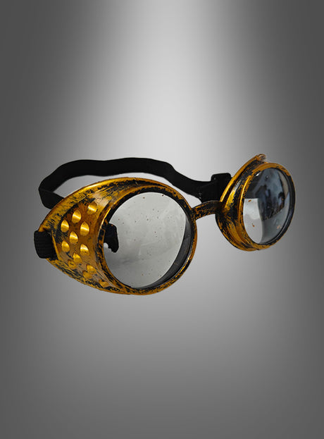 Ein Paar goldene Steampunk-Schweißerbrillen mit runden, klaren Gläsern im Vintage-Stil, einem schwarzen Riemen und strukturierten Seitenteilen – perfekt als Steampunk-Brille oder als Blickfang für Ihr Steampunk-Kostüm – präsentiert vor einem grauen Hintergrund mit Farbverlauf.