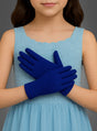 Ein junges Mädchen in einem hellblauen, ärmellosen Kleid steht mit vor der Taille verschränkten Händen da und präsentiert ihre „Blaue Handschuhe für Kinder“ – ein perfektes Accessoire für Kinderkostüme, das ihrem Outfit eine verspielte Note verleiht.