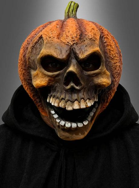 Eine Person, die die „Kürbis-Maske“ – eine lachende Totenkopfmaske aus Latex – und einen schwarzen Kapuzenmantel trägt, blickt vor einem schlichten grauen Hintergrund nach vorne.