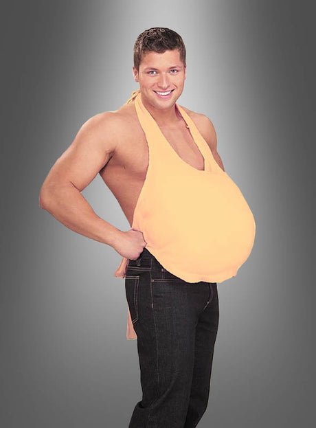 Ein Mann in Jeans und einem pfirsichfarbenen Neckholder-Top posiert vor einem grauen Hintergrund mit Farbverlauf und präsentiert auf humorvolle Weise den „Bierbauch-Attrappe – wattierter Bauch“ – ein naturgetreues, gepolstertes Bauchkostüm, das sich perfekt für lustige Herrenoutfits eignet.