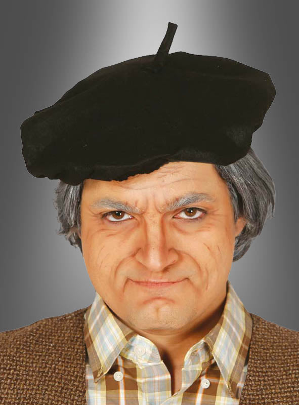 Eine Person mit einer schwarzen Baskenmütze, einer grauen Perücke, einem karierten Hemd und einer braunen Weste blickt mit ausdruckslosem Gesicht in die Kamera vor einem grauen Hintergrund mit Farbverlauf – für einen zusätzlichen Hauch von französischem Flair.