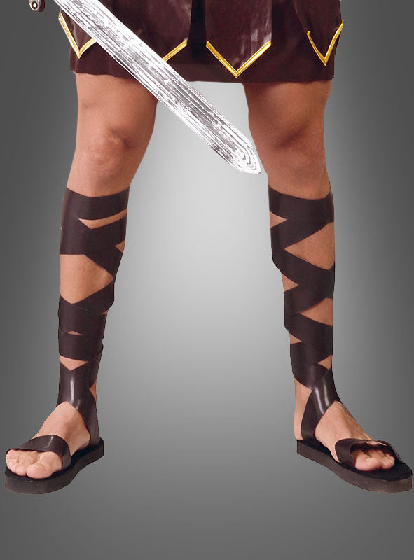 Eine Person, die Römersandalen und Schienbeinschoner trägt, ein Schwert in der Hand hält und vor einem grauen Hintergrund nur mit den Beinen zu sehen ist – perfekt, um eine authentische Gladiator-Verkleidung zu kreieren.