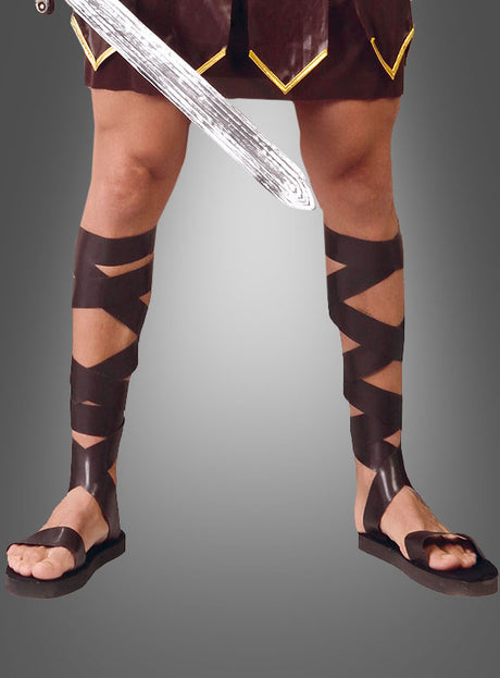 Eine Person, die Römersandalen und Schienbeinschoner trägt, ein Schwert in der Hand hält und vor einem grauen Hintergrund nur mit den Beinen zu sehen ist – perfekt, um eine authentische Gladiator-Verkleidung zu kreieren.