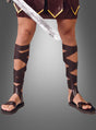 Eine Person, die Römersandalen und Schienbeinschoner trägt, ein Schwert in der Hand hält und vor einem grauen Hintergrund nur mit den Beinen zu sehen ist – perfekt, um eine authentische Gladiator-Verkleidung zu kreieren.
