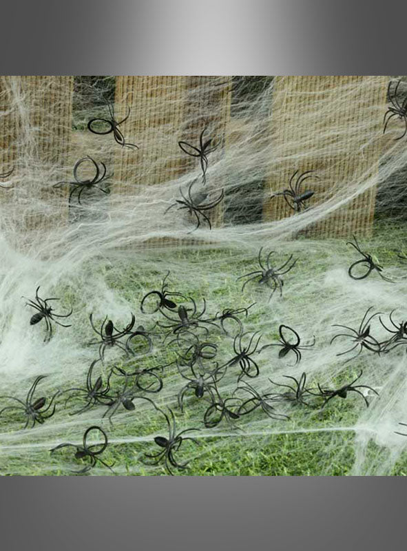 Schwarze Spinnen mit Ring-Dekor sind auf künstlichen Spinnennetzen verteilt, die über Gras und Holzbretter drapiert sind, und sorgen so für eine klassische Halloween-Dekoration oder eine gruselige Dekorationskulisse.
