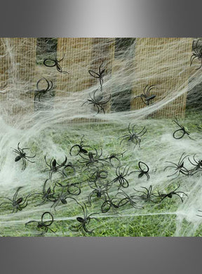 Schwarze Spinnen mit Ring-Dekor sind auf künstlichen Spinnennetzen verteilt, die über Gras und Holzbretter drapiert sind, und sorgen so für eine klassische Halloween-Dekoration oder eine gruselige Dekorationskulisse.