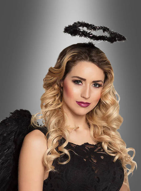 Eine Frau mit langen blonden Locken trägt ein schwarzes Engelskostüm aus Spitze, schwarze Engelsflügel und den schwarzen Heiligenschein für gefallene Engel und posiert vor einem grauen Hintergrund mit Farbverlauf.