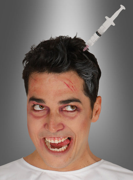 Ein Mann mit Make-up, das wie blaue Flecken und Schnittwunden aussieht, lächelt breit und trägt den „Haarreif mit Spritze im Kopf Unisex“, der die gruselige Illusion einer in seinem Haar steckenden Spritze erzeugt – perfekt, um bei jedem Zombie-Walk einen Horror-Kostüm-Effekt zu erzielen.