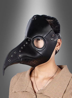 Eine Person, die die „Deluxe Pest Maske“ trägt – gefertigt aus schwarzem Kunstleder mit runden Glasaugenöffnungen und Nietenverzierungen –, steht vor einem grauen Hintergrund mit Farbverlauf.
