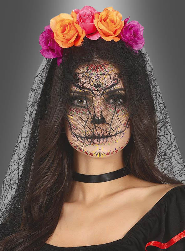 Eine Frau mit „Dia de los Muertos“-Gesichtsbemalung trägt einen schwarzen Schleier, ein mit orangefarbenen und violetten Blumen verziertes Blumen-Haarband mit Spinnennetz-Schleier sowie ein schwarzes Halsband vor grauem Hintergrund.