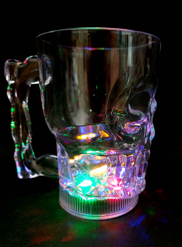 Ein Totenkopf-Krug aus klarem Glas (500 ml) mit Henkel und LED, der die Form eines Totenkopfs hat, steht auf einer schwarzen Unterlage und wird von unten durch leuchtende LED-Lichter beleuchtet – damit ist er der perfekte Halloween-Becher für Ihre nächste gruselige Feier.