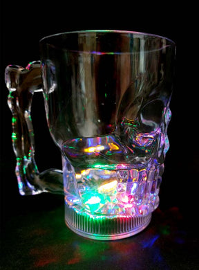 Ein Totenkopf-Krug aus klarem Glas (500 ml) mit Henkel und LED, der die Form eines Totenkopfs hat, steht auf einer schwarzen Unterlage und wird von unten durch leuchtende LED-Lichter beleuchtet – damit ist er der perfekte Halloween-Becher für Ihre nächste gruselige Feier.