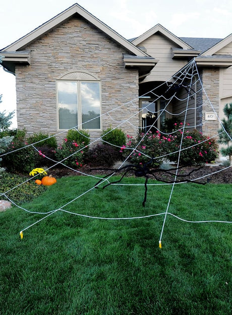 Das 5 Meter lange Spinnennetz – eine riesige Halloween-Dekoration – schmückt kunstvoll den Vorgarten eines Hauses, ausgebreitet mit einer großen schwarzen Spinne und umgeben von Kürbissen sowie Blumen am Eingang – eine beeindruckende Halloween-Dekoration.