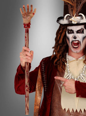 Eine Person in einem theatralischen Voodoo-Kostüm und einem aufwendigen Hut hält mit auffälliger Gesichtsbemalung dramatisch den 70 cm langen Dolch mit der blutigen, abgetrennten Hand als Halloween-Accessoire in der Hand und zeigt vor einem farbenprächtigen Hintergrund mit Farbverlauf darauf.