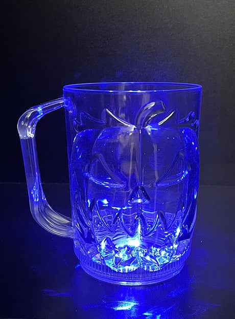 Der „Großer Halloween-Kürbis-Krug LED 700 ml“ ist ein durchsichtiger Kunststoffbecher mit einem Kürbisgesicht-Motiv, der von unten mit blauen LED-Lichtern beleuchtet wird und vor einem dunklen Hintergrund steht.