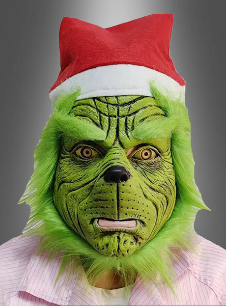 Eine Person, die die „Grüne Maske Weihnachtsmonster“-Halbmaske trägt, mit einer Weihnachtsmannmütze und einem hellen Hemd, vor einem grauen Hintergrund.