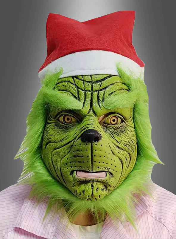 Eine Person, die die „Grüne Maske Weihnachtsmonster“-Halbmaske trägt, mit einer Weihnachtsmannmütze und einem hellen Hemd, vor einem grauen Hintergrund.