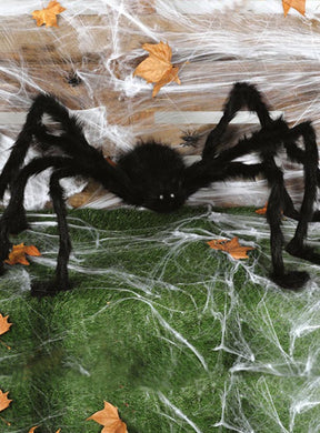 Überlebensgroße Spinne (150 cm) mit LED-Augen in Schwarz auf grünem Gras, mit weißen künstlichen Spinnweben und verstreuten Herbstblättern – perfekt als Halloween-Spinne oder gruselige Spinnendekoration für Ihre festliche Dekoration.