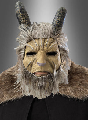 Vor einem grauen Farbverlaufshintergrund ist eine Person zu sehen, die die „Biest Vollmaske mit Hörner Krampus“ trägt, die mit ziegenartigen Hörnern, Fellverzierungen und einem braunen Umhang ausgestattet ist.