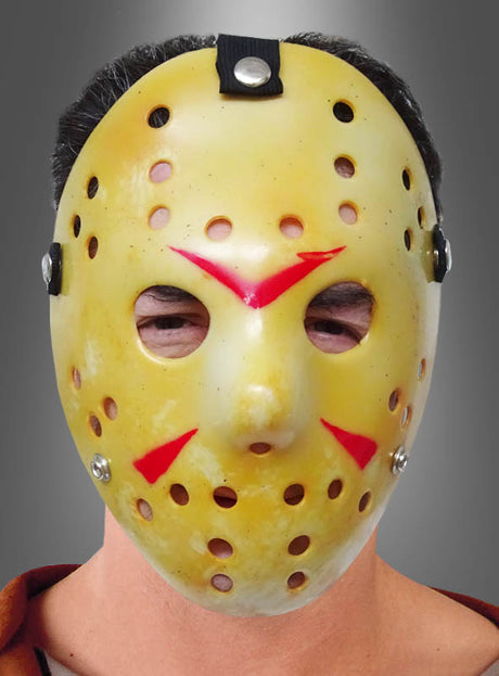 Eine Person, die die gelbe „Horror Hockey“-Maske für Halloween mit roten Markierungen und zahlreichen Belüftungslöchern trägt, blickt nach vorne. Diese furchterregende Halloween-Maske ist ideal für alle, die den klassischen „Hockeymaskenmörder“-Stil lieben.
