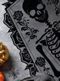 Mit einem schwarzen Skelett- und Rosenmotiv auf dunklem Stoff, akzentuiert durch einen goldenen Kürbis, eine Spinne und Geschirr auf einem strukturierten grauen Hintergrund, ist der Tischläufer „Skelett“ 183 x 60 cm Halloween die ideale Halloween-Dekoration, um Ihrem Essbereich im Handumdrehen einen stilvollen, gruseligen Touch zu verleihen.