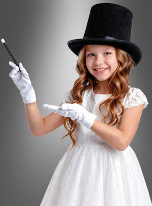Ein lächelndes Mädchen in einem weißen Kleid und weißen Handschuhen steht vor einem grauen Hintergrund mit Farbverlauf und trägt das „Zauberer-Set für Kinder mit Zylinder“ – bestehend aus einem Zylinder und einem Zauberstab – als Teil ihres Zaubererkostüms.