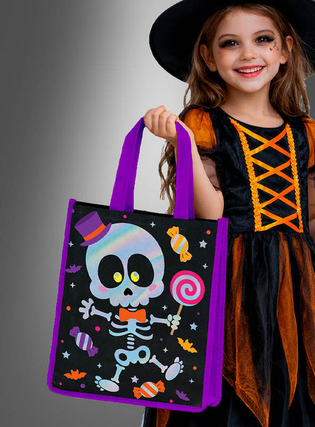 Ein lächelndes Kind in einem Hexenkostüm hält die Halloween-Sammeltasche „Lustiges Skelett“ in der Hand, die mit einem Comic-Skelett, Bonbons und Fledermäusen verziert ist – bereit, leckere Halloween-Süßigkeiten zu sammeln.