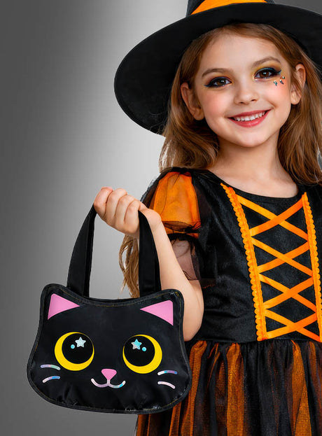 Ein kleines Mädchen in einem Hexenkostüm lächelt in die Kamera, während es die Halloween-Handtasche „Süße Katze“ vor einem grauen Farbverlaufshintergrund in den Händen hält. Diese entzückende Katzentasche ist das perfekte Kostüm-Accessoire für Kinder für jeden zauberhaften Anlass.