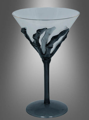 Ein transparentes Cocktailglas „Skeletthand“ (18 cm) mit schwarzem Stiel und einem auffälligen Skeletthand-Motiv, das sich um den Kelch windet, vor einem grau verlaufenden Hintergrund – perfekt als einzigartiger Blickfang für Ihre Halloween-Party oder als auffällige Halloween-Dekoration.