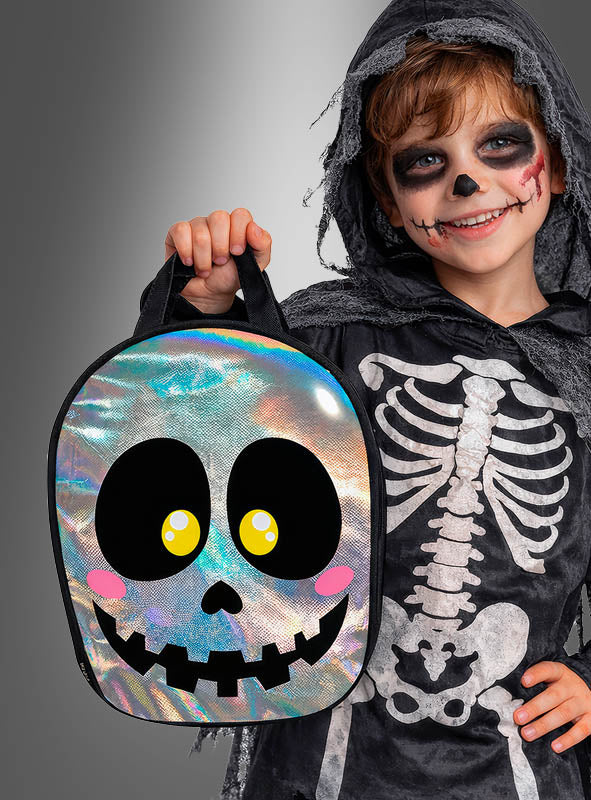 Ein Kind in einem Skelettkostüm mit Gesichtsbemalung hält eine glänzende „Halloween-Tasche in Form eines schillernden Totenkopfs“ in der Hand, die mit Comic-Augen und einem lächelnden Mund verziert ist – ein ideales Kinderaccessoire für gruselige Feste.