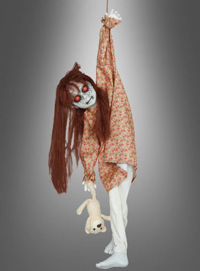 Die „Hängende Horror-Puppe“ (90 cm) hat langes braunes Haar, rote Augen und trägt ein geblümtes Kleid. Sie hängt an einem Arm und hält einen Teddybären fest, vor einem grauen Hintergrund – eine beunruhigende, animierte Halloween-Dekoration, die Ihren Gästen garantiert Gänsehaut bereiten wird.