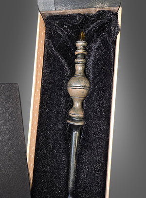 Ein Zauberstab Deluxe in einer Geschenkschachtel mit einem kunstvoll gearbeiteten Griff ruht in einer mit schwarzem Samt ausgekleideten Geschenkbox und weckt Erinnerungen an den legendären Harry-Potter-Zauberstab aus der berühmten Zauberschule.