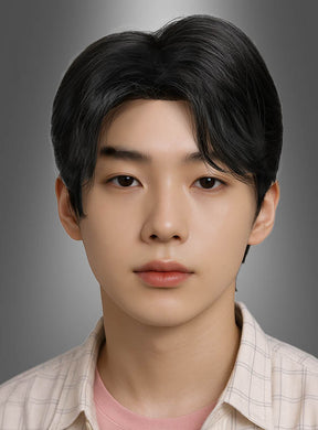 Ein junger Mensch mit glattem, dunklem Haar, das im Stil der Boy-Group-Sänger-Perücke aus dem K-Pop frisiert ist, und mit makelloser Haut blickt vor einem neutralen grauen Hintergrund nach vorne; er trägt ein helles Karohemd über einem rosa Oberteil.