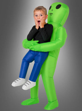 Ein Kind trägt das „aufblasbare Alien-Kostüm für Kinder“ und erweckt den Eindruck, von einem großen grünen aufblasbaren Alien gehalten zu werden, mit einem überraschten Gesichtsausdruck vor einem neutralen Hintergrund mit Farbverlauf.