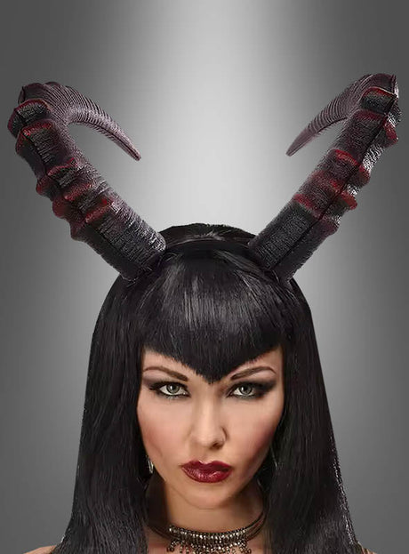 Eine Frau mit langen schwarzen Haaren und auffälligem Make-up trägt einen strukturierten, schwarz-roten „Hörner“-Haarreif (Cosplay, Unisex) als markantes Halloween-Accessoire auf dem Kopf, vor einem grau verlaufenden Hintergrund.