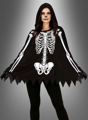 Eine Person im „Skelett-Poncho“-Halloween-Kostüm – bestehend aus einem schwarzen Poncho mit weißem Skelett-Aufdruck und Kapuze – steht mit einem als Totenkopf geschminkten Gesicht vor einem grau verlaufenden Hintergrund – eine ideale Wahl für Halloween-Kostüme für Damen bei jeder gruseligen Feier.