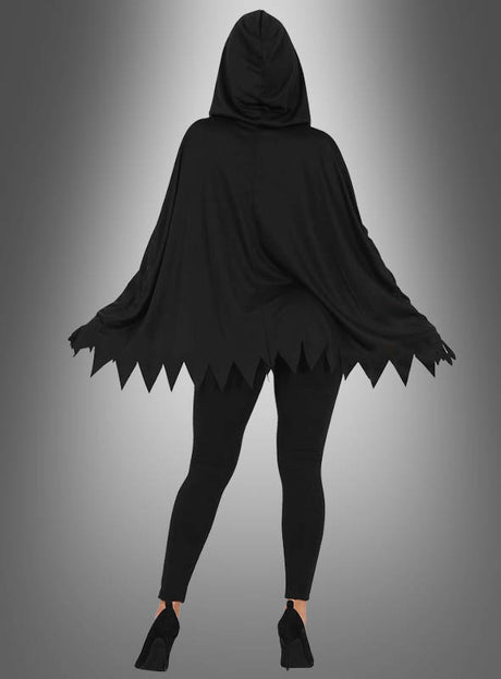 Eine Person, die das „Skelett-Poncho“-Halloween-Kostüm trägt – einen schwarzen Umhang mit Kapuze und gezackten Rändern –, kombiniert mit schwarzen Leggings und schwarzen Pumps, steht vor einem grauen Hintergrund mit Farbverlauf.