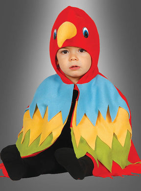 Ein kleines Kind sitzt vor einem grauen Hintergrund und trägt das „Kleiner Papagei“-Babykostüm, das aus einer roten Kapuze mit gelbem Schnabel, blauen Flügeln und gelbgrünen Federn besteht.
