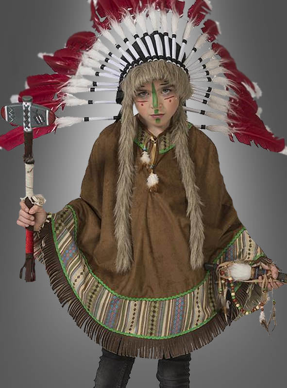Eine Person in einem Kostüm im Stil der amerikanischen Ureinwohner mit Federkopfschmuck und Gesichtsbemalung, die einen Tomahawk und eine Rassel in den Händen hält, steht vor einem grauen Hintergrund – bekleidet mit dem „Indianer-Poncho für Mädchen und Jungs“, der sich perfekt für jeden Anlass im Stil des Wilden Westens eignet.